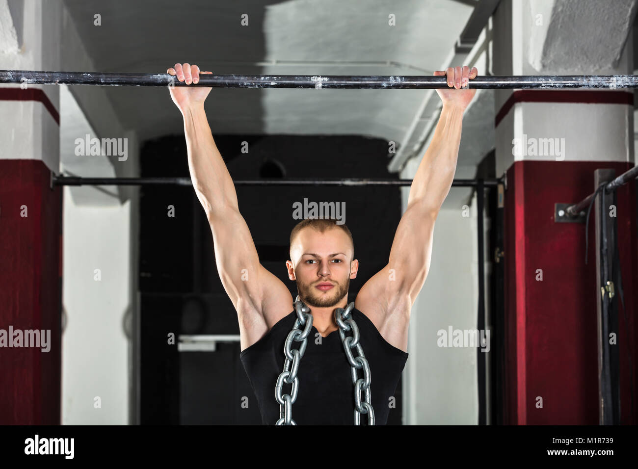 Atleta hombre vestido con una cadena de metal haciendo Pull-ups en la barra horizontal en el gimnasio. Foto de stock