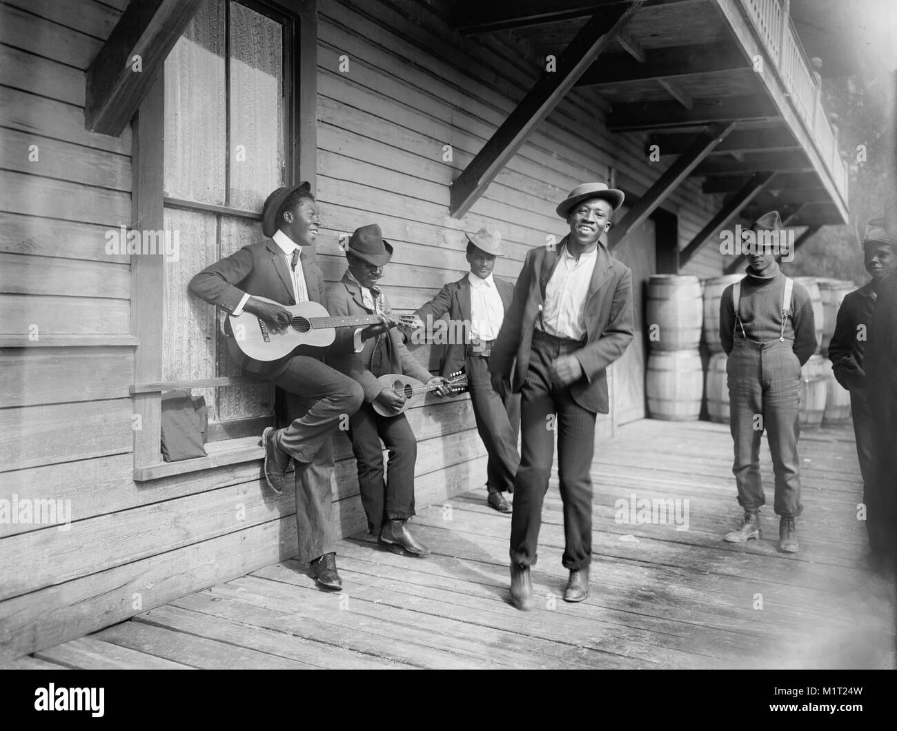 Grupo de hombres jugando música y baile en el porche, 'Esperando el domingo Boat", William Henry Jackson para Detroit Publishing Company, 1902 Foto de stock