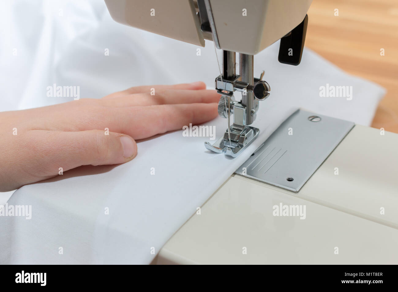Close-up de una mano blanca líder childs textil a través de una máquina de coser Foto de stock