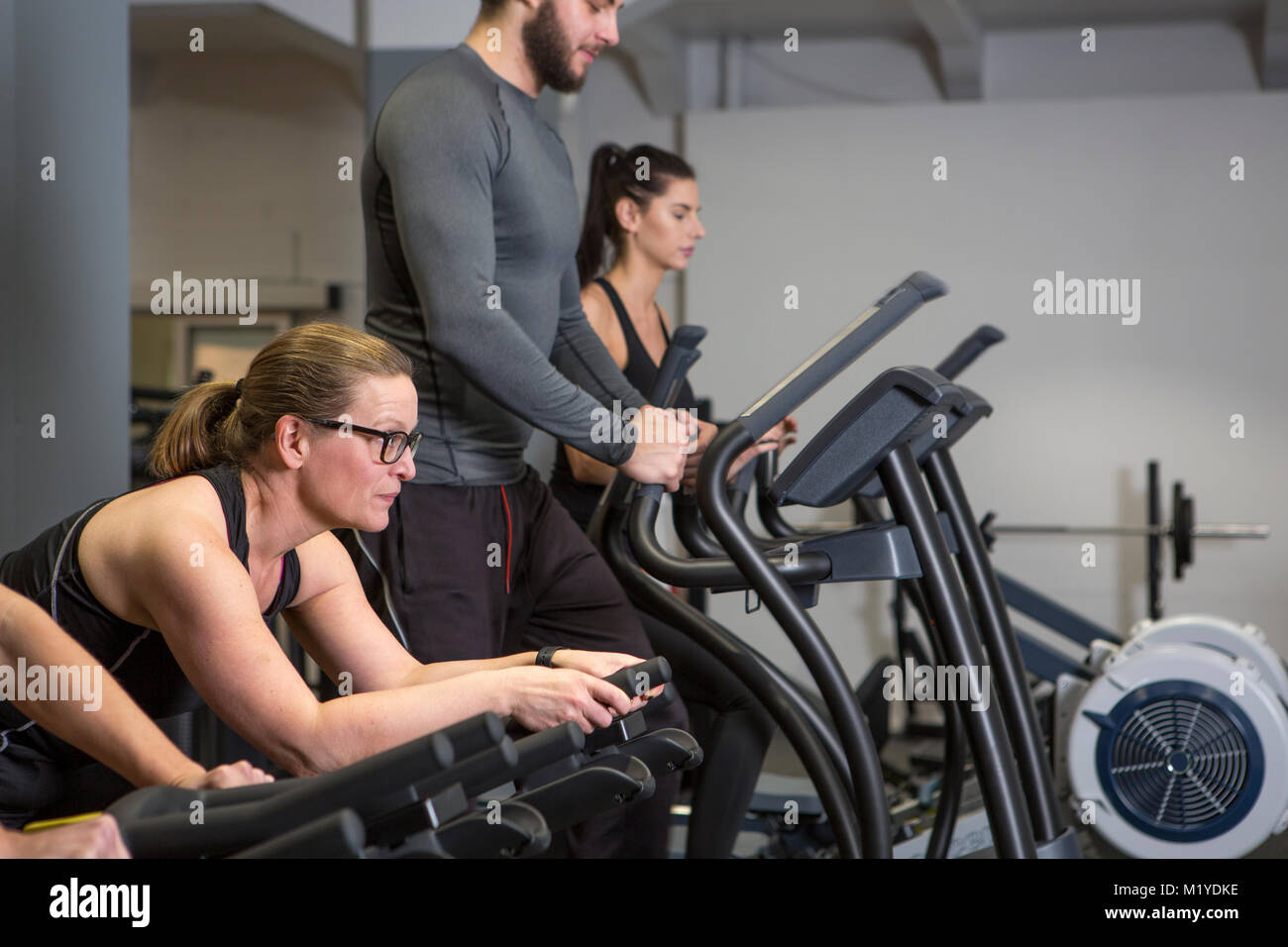 Tres mujeres y un hombre a entrenar en un gimnasio con máquinas de cardio. Todas tienen expresiones felices. Foto de stock