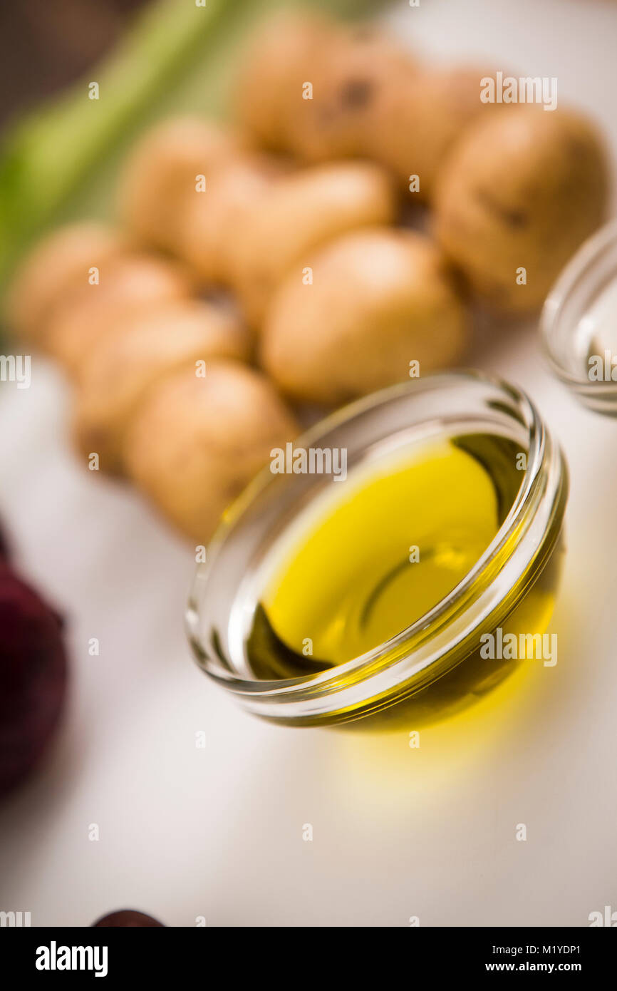 Pequeño recipiente con aceite de oliva en la parte delantera de patatas y verduras Foto de stock