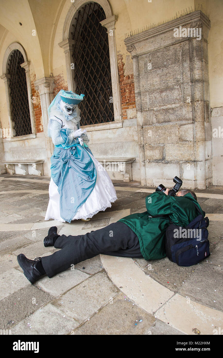 El fotógrafo toma fotografías de máscara veneciana tumbado en el suelo con cámara DSLR, la Plaza de San Marcos en Venecia. Foto de stock
