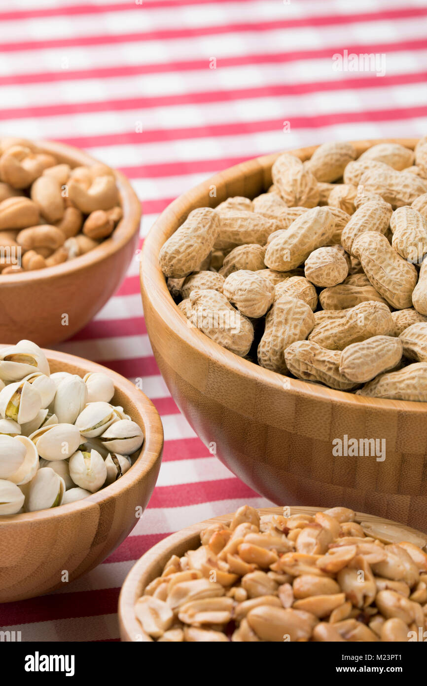 Cerca de la parte tazones de cacahuetes, almendras, pistachos y anacardos sobre un mantel rojo a cuadros Foto de stock