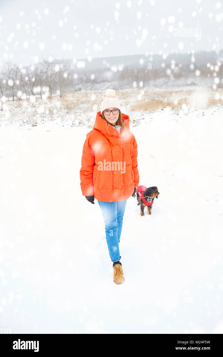 Disparo de longitud completa de una mujer alegre y caminar su perro pequeño al aire libre en invierno. Foto de stock