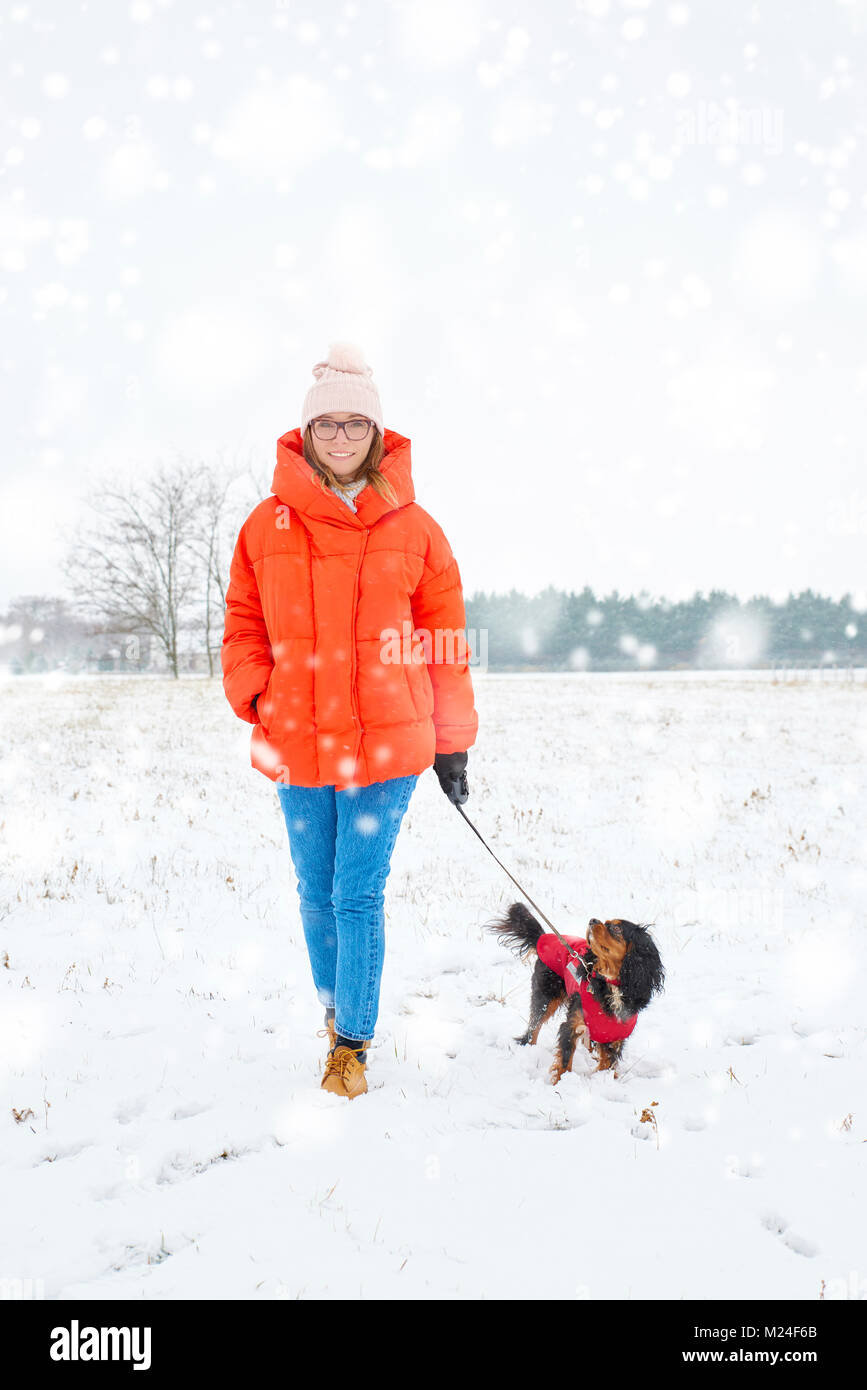 Disparo de longitud completa de una mujer alegre y caminar su perro pequeño al aire libre en invierno. Foto de stock