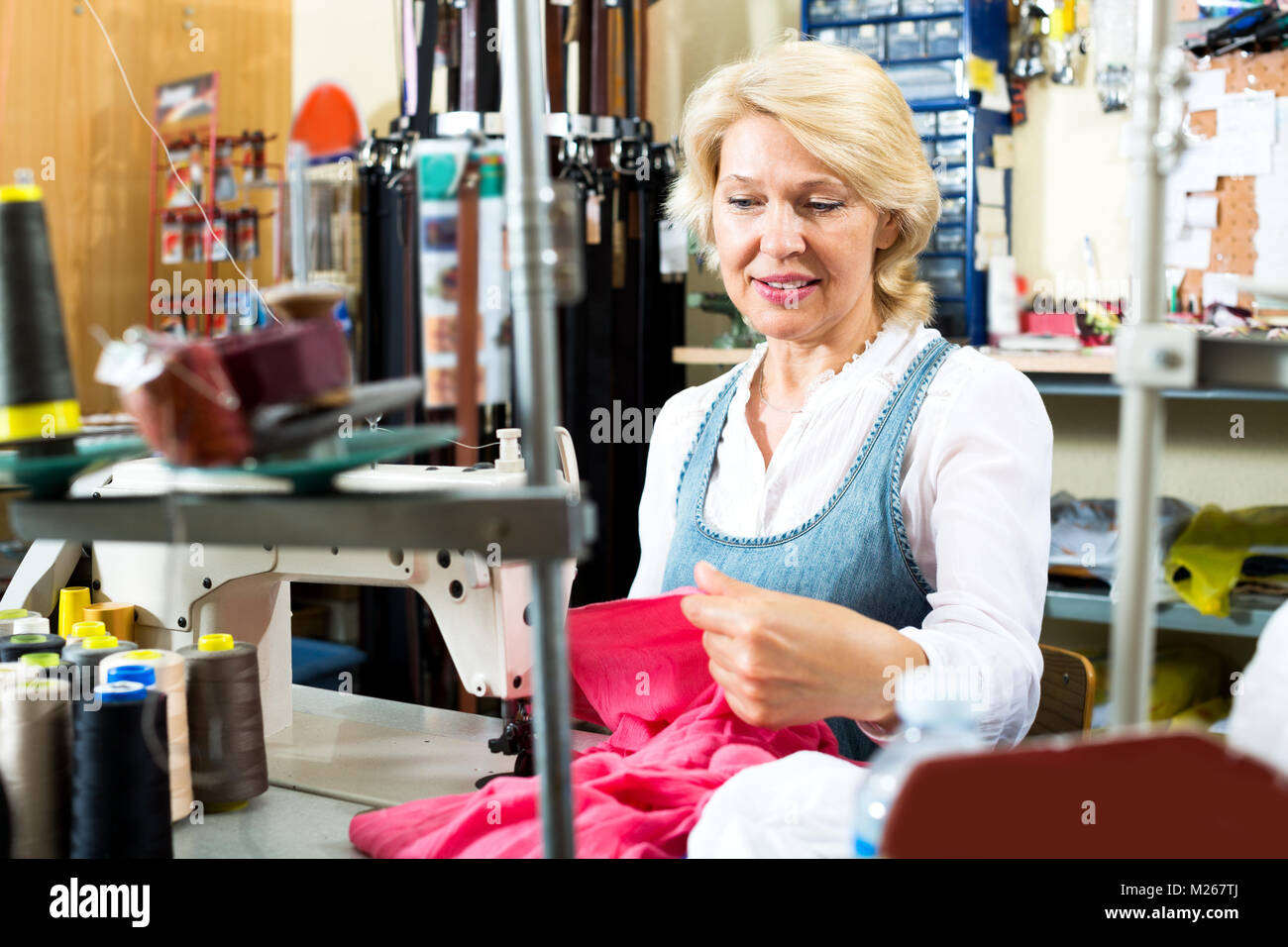 Feliz mujer madura coser con máquina profesional en un taller Foto de stock