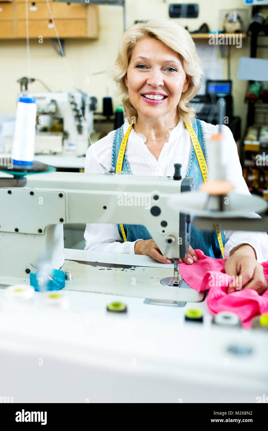Alegre mujer senior coser con máquina profesional en un taller Foto de stock