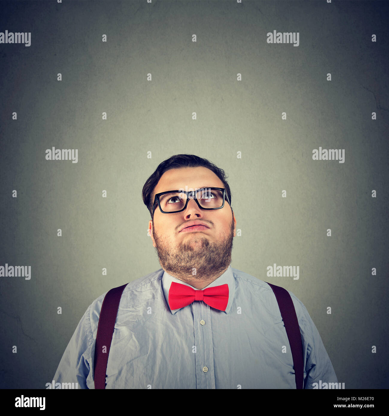 Joven hombre gordito en pajarita mirando hacia arriba en el aburrimiento posando sobre fondo gris. Foto de stock