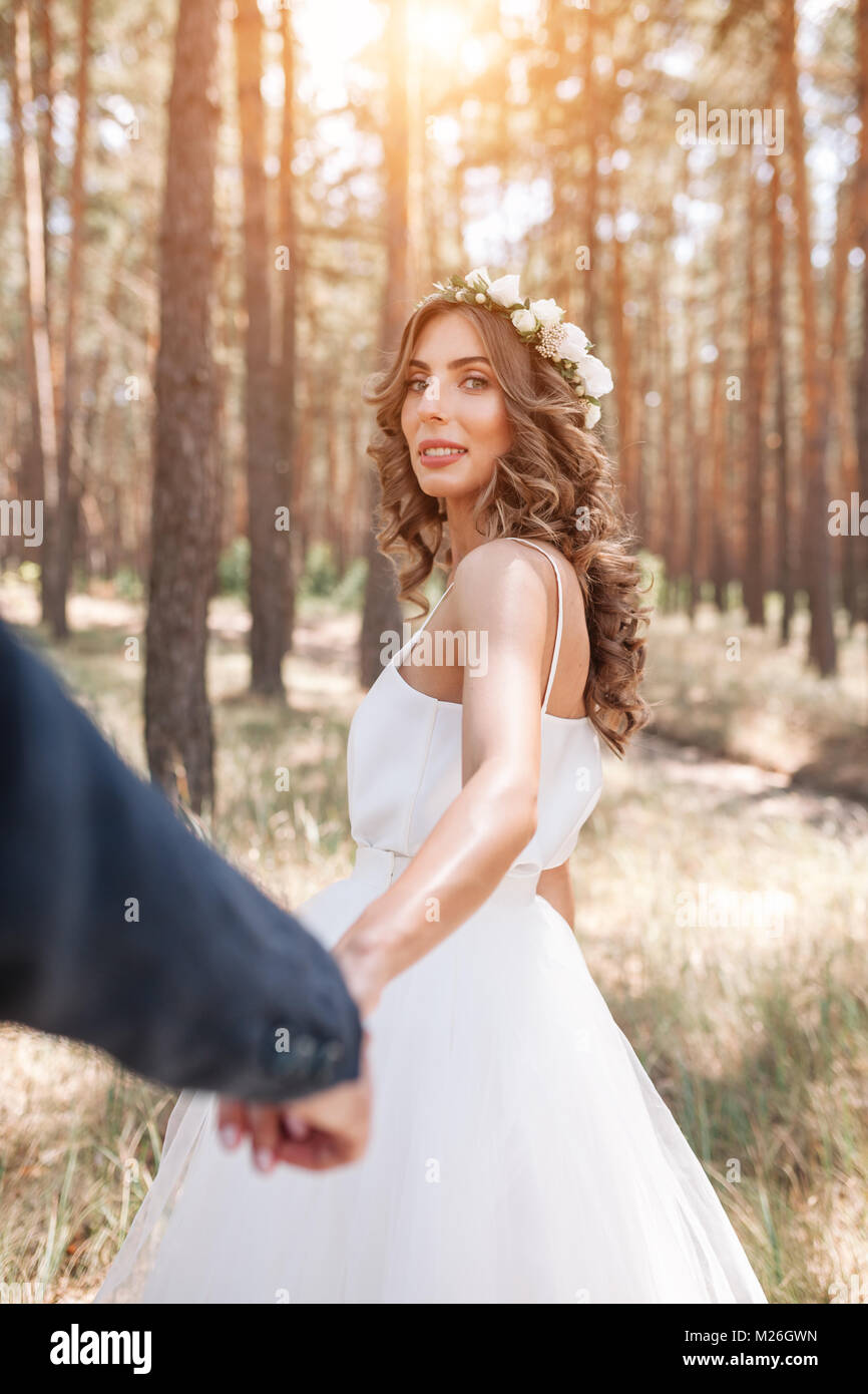 Una niña hermosa novia sostiene la mano de su fhand y lo conduce hacia el bosque de pinos siga en mí Foto de stock
