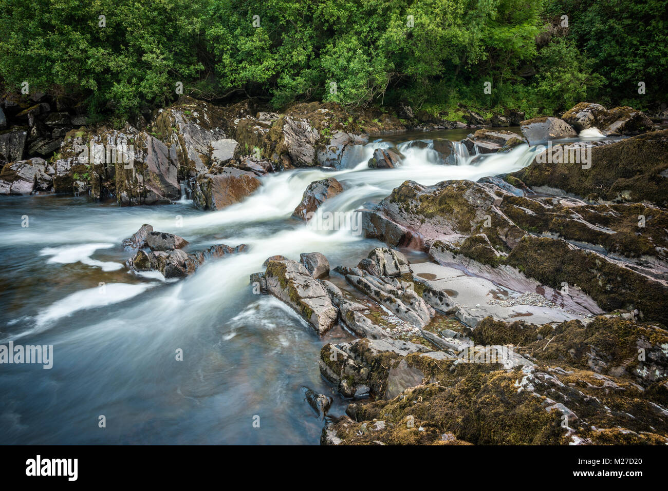 Río que fluye sobre rocas con agua borrosa Foto de stock