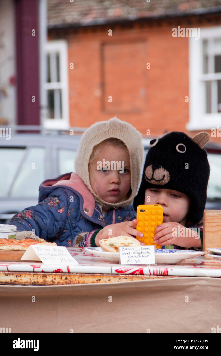 Dos niños en tejido pasamontañas en un puesto de comida messing con un  teléfono móvil de color amarillo brillante Fotografía de stock - Alamy