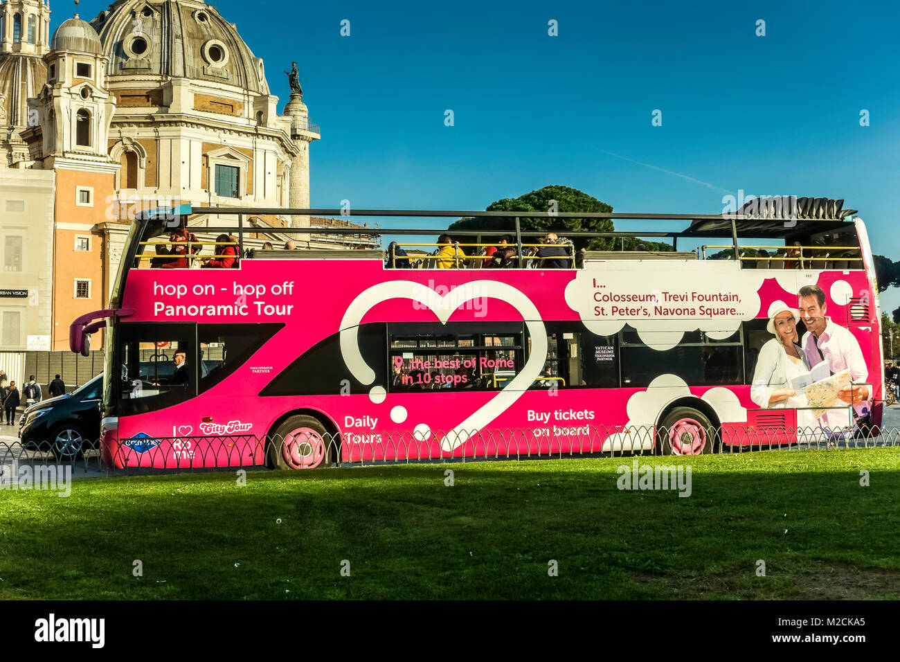 Visitas turísticas, hop on hop off, Rosa double decker bus pasando por la plaza de Venecia. Roma, Italia, Europa. El azul claro del cielo, espacio de copia. Vista lateral. Foto de stock