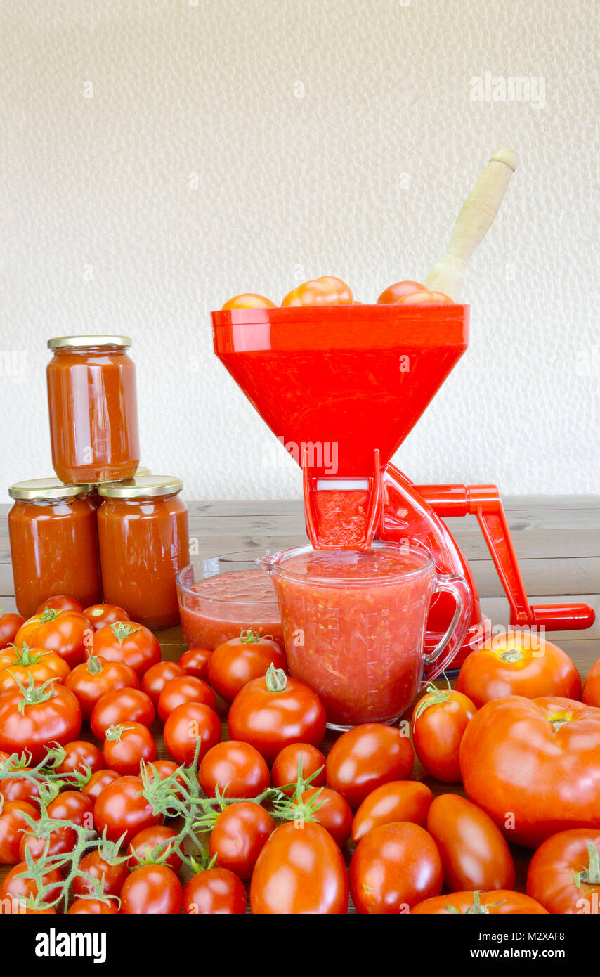 Colador de tomate, los tomates frescos, frescos y salsa de tomate enlatado  y envasado en una mesa de madera Fotografía de stock - Alamy