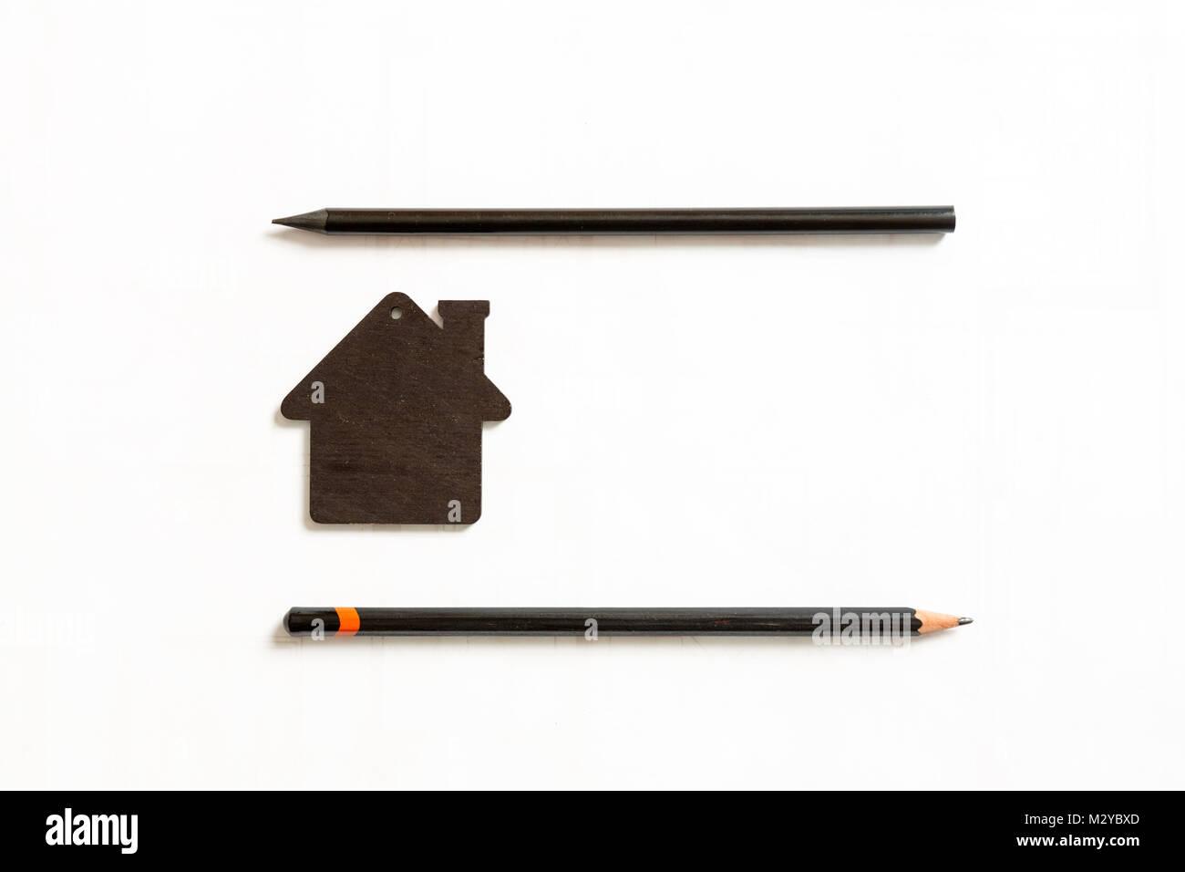 Imagen del modelo negro pequeño de una casa con lápices de color negro sobre un fondo blanco. Foto de stock