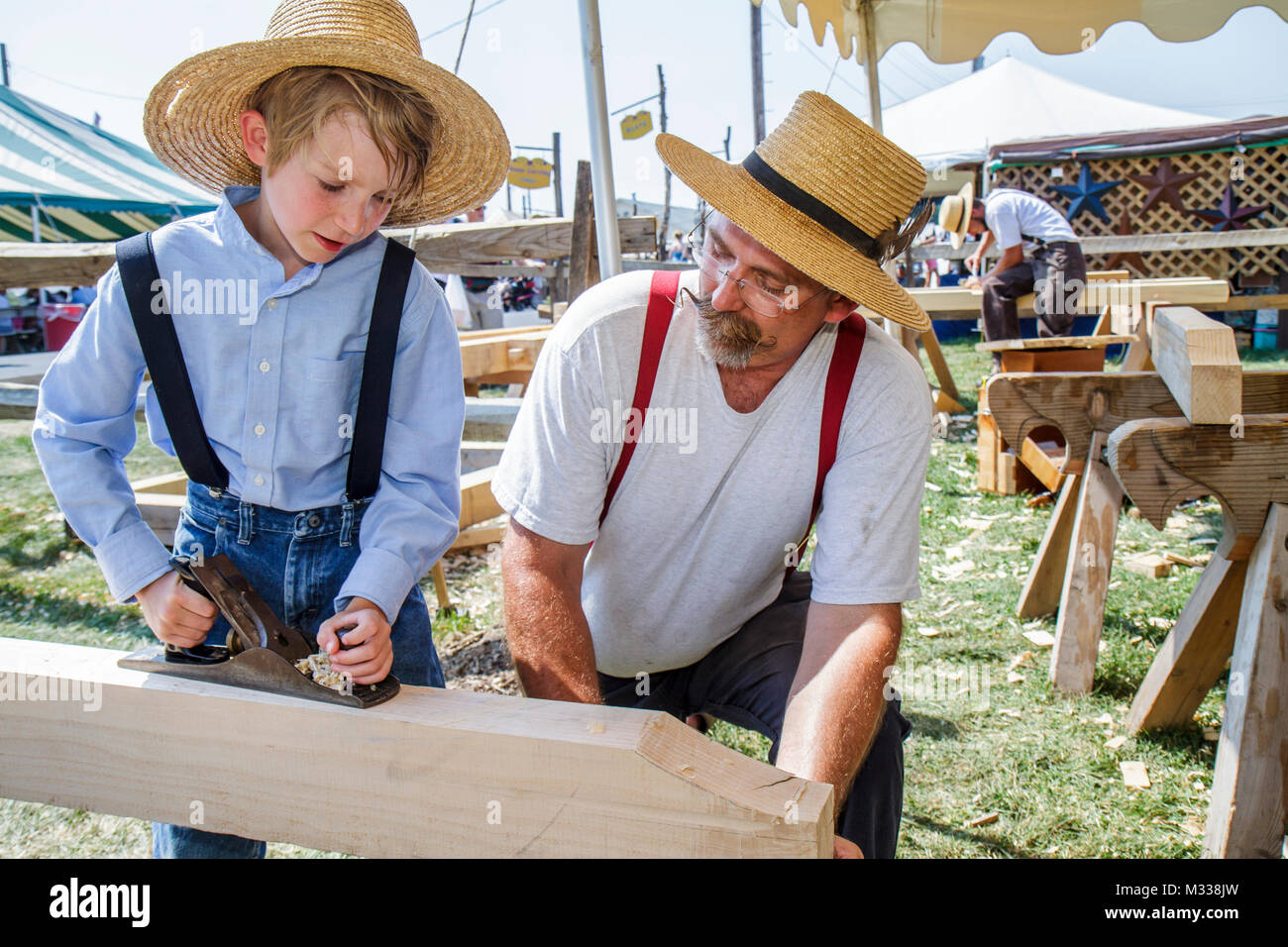 Kutztown Folk Festival, Pennsylvania Holandes folklife Amish, hombre niño padre hijo, carpintero, madera herramienta de avión enseñar sombrero de paja con tirantes Foto de stock