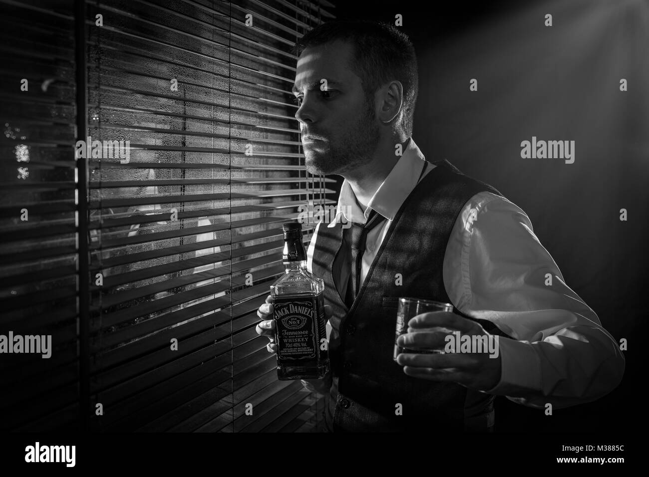 Gángster sosteniendo una botella de whisky y vidrio mientras mira por la  ventana Fotografía de stock - Alamy