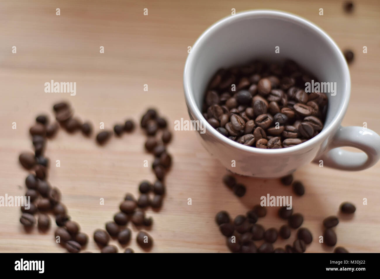Taza llena de granos de café/ Forma corazón de granos de café en la mesa de madera/ vista superior Foto de stock
