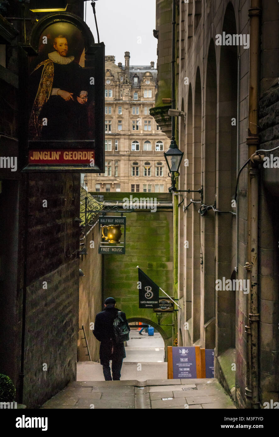 Hombre caminando en el estrecho callejón con Jinglin Fleshmarket Geordie y Halfway House pub signos, Edimburgo, Escocia, Reino Unido, con el Balmoral Hotel en distancia Foto de stock