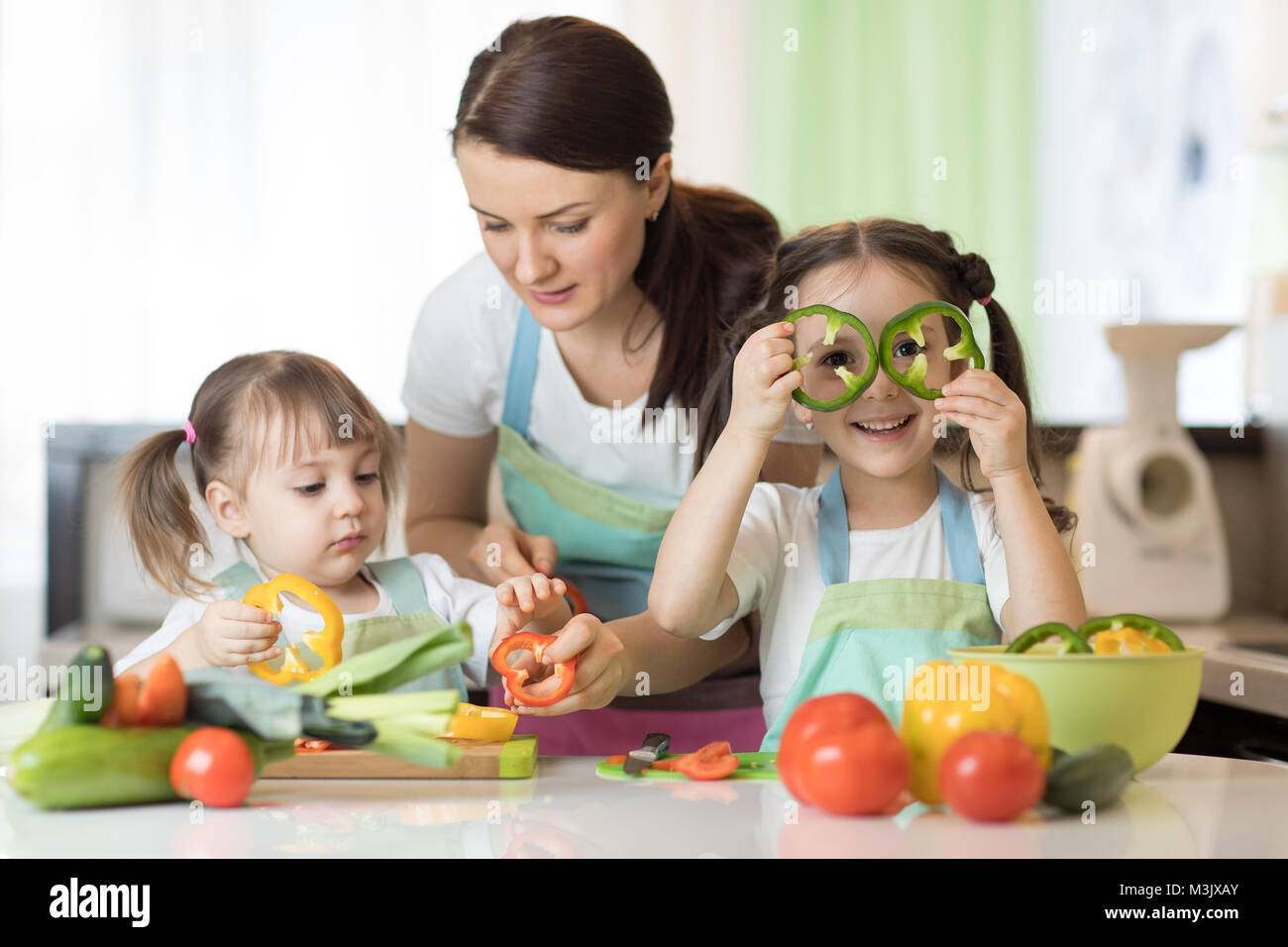 Mamá enseña dos hijas para cocinar en la mesa de la cocina con alimentos  crudos Fotografía de stock - Alamy