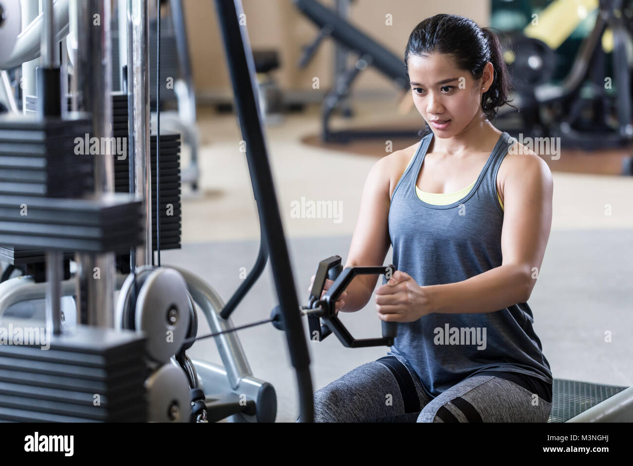 Retrato de una fuerte y hermosa joven sentado mientras que el remo en el  cable de la máquina para músculos de la espalda durante el intenso  entrenamiento en el gimnasio Fotografía de