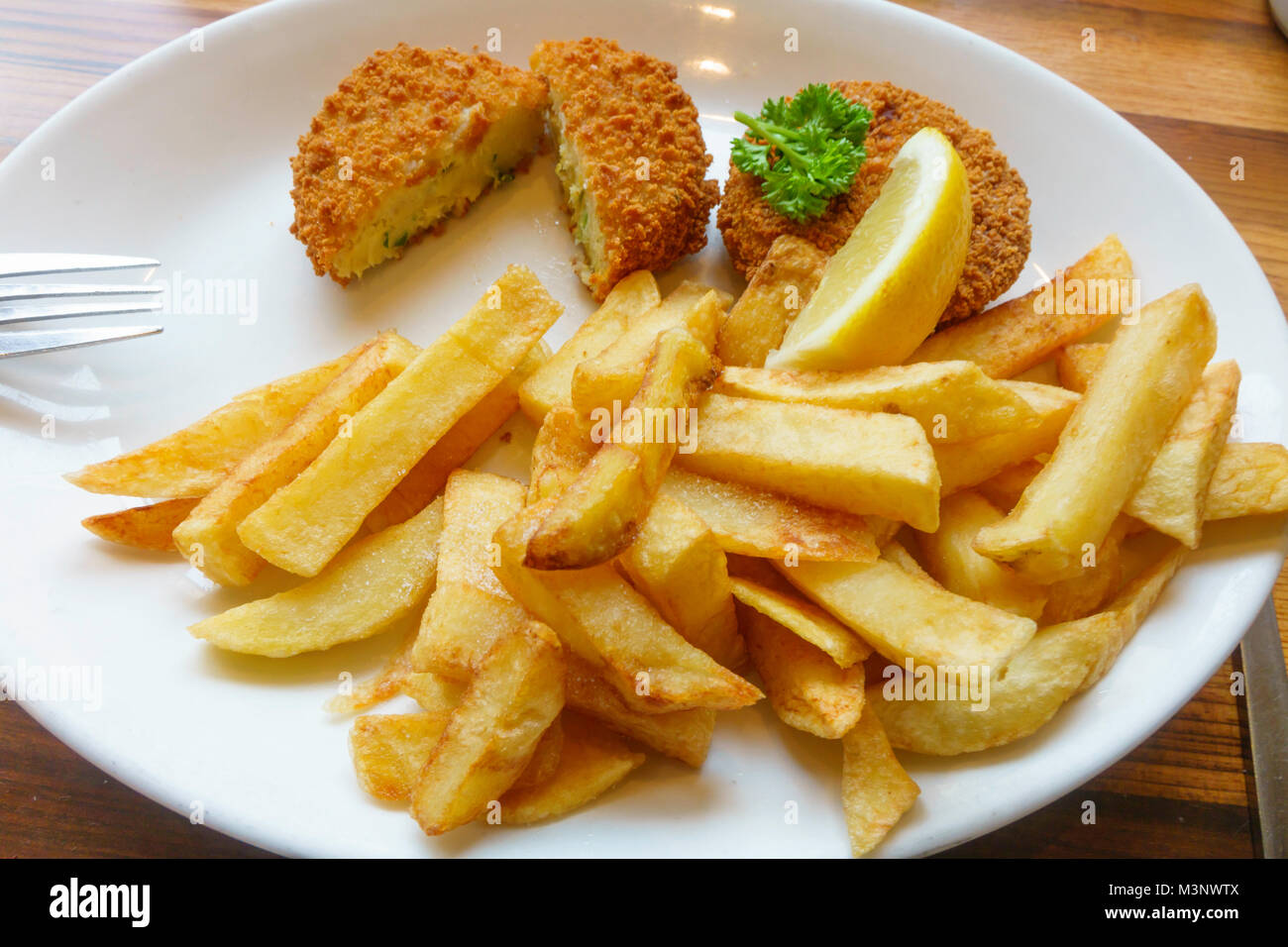 Almuerzo en un café de abadejo ahumado hamburguesas de pescado con papas fritas y una rodaja de limón perejil decorar pastel de pescado cortados Foto de stock