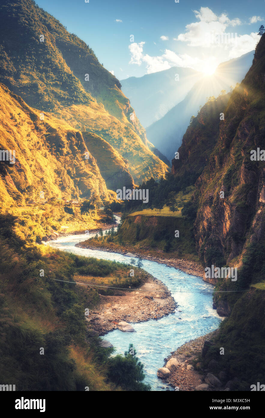 Coloridos paisajes con altas montañas del Himalaya, hermoso río curvada, verde bosque, el cielo azul con nubes y amarillo sol al atardecer en otoño Foto de stock