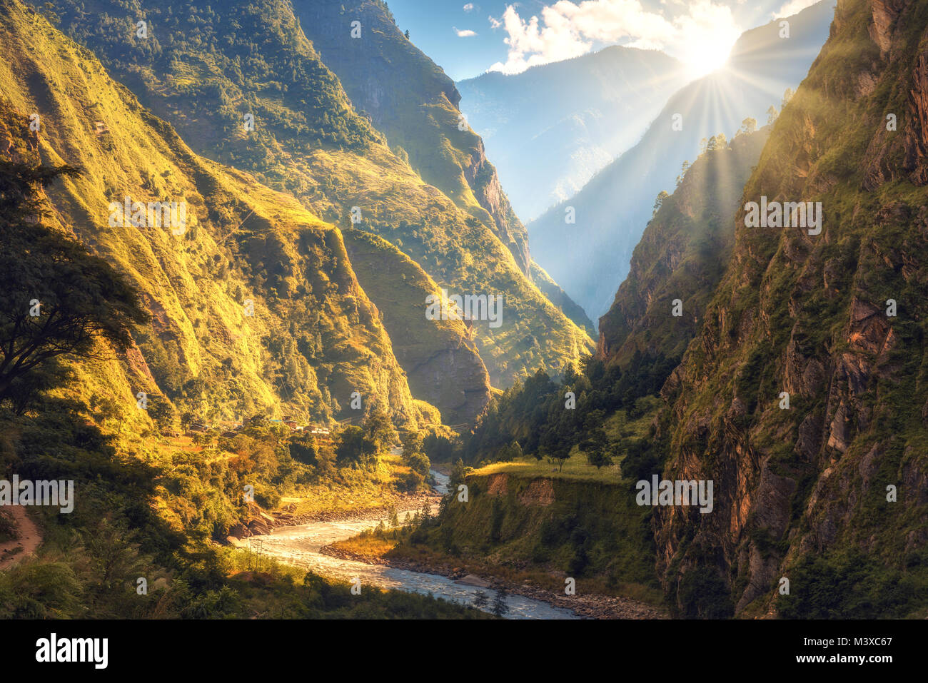 Coloridos paisajes con altas montañas del Himalaya, hermoso río curvada, verde bosque, el cielo azul con nubes y amarillo sol al atardecer en otoño Foto de stock