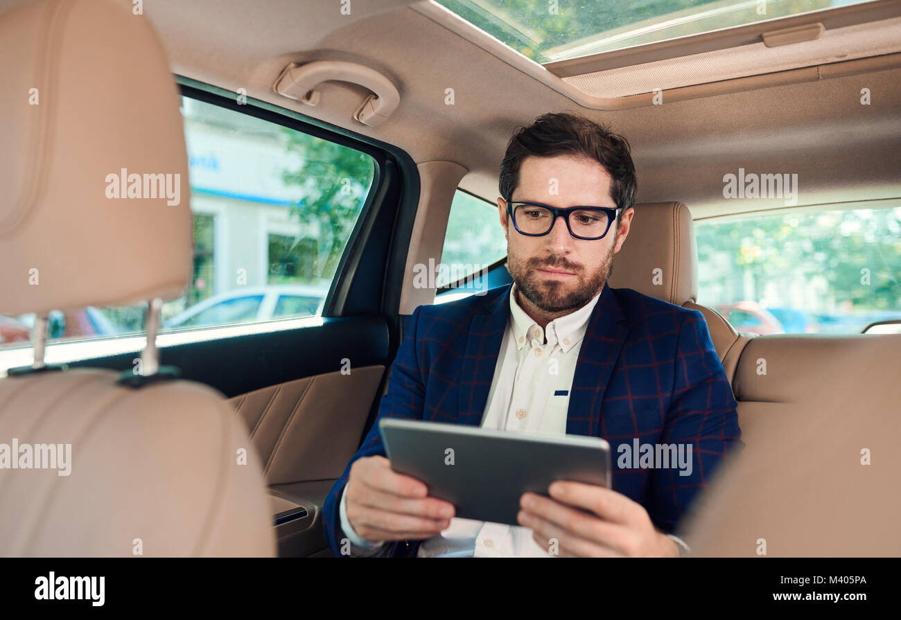 Joven empresario exitoso utilizando una tableta digital en su coche Foto de stock
