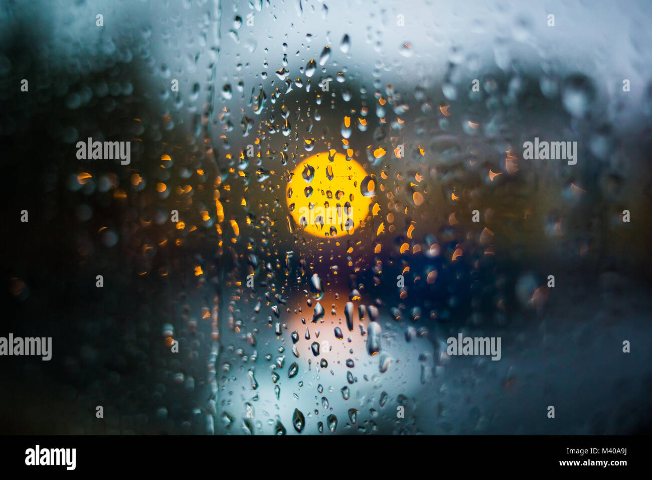 Las gotas de lluvia en la ventana. Tarde o noche tranquila en casa cuando llueve fuera. Gotas de agua sobre el vidrio. Superficie de vidrio mojado. Salpicaduras de agua. Las luces de la ciudad de bo Foto de stock