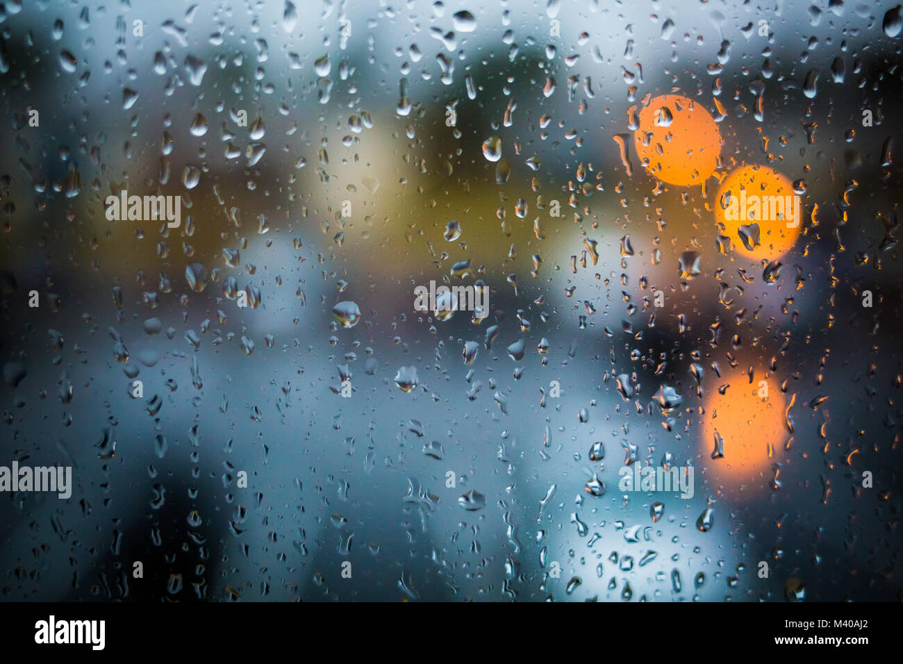 Las gotas de lluvia en la ventana. Tarde o noche tranquila en casa cuando llueve fuera. Gotas de agua sobre el vidrio. Superficie de vidrio mojado. Salpicaduras de agua. Las luces de la ciudad de bo Foto de stock