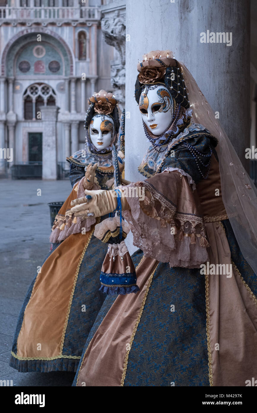 Dos mujeres cosidas a mano trajes y máscaras pintadas a mano, decoradas con  ventiladores, de pie en frente de los arcos en San marco durante el  Carnaval de Venecia Fotografía de stock -