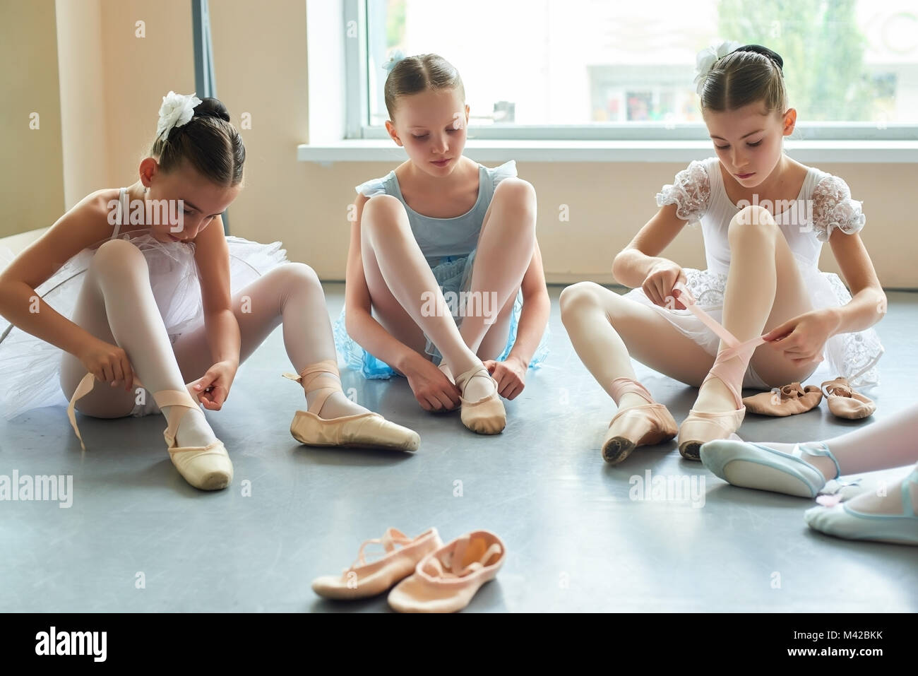 Preparación para niños ballet. Tres jóvenes bailarines sentados en el suelo y en los zapatos de ballet. Concepto de ballet y coreografía Fotografía de stock - Alamy