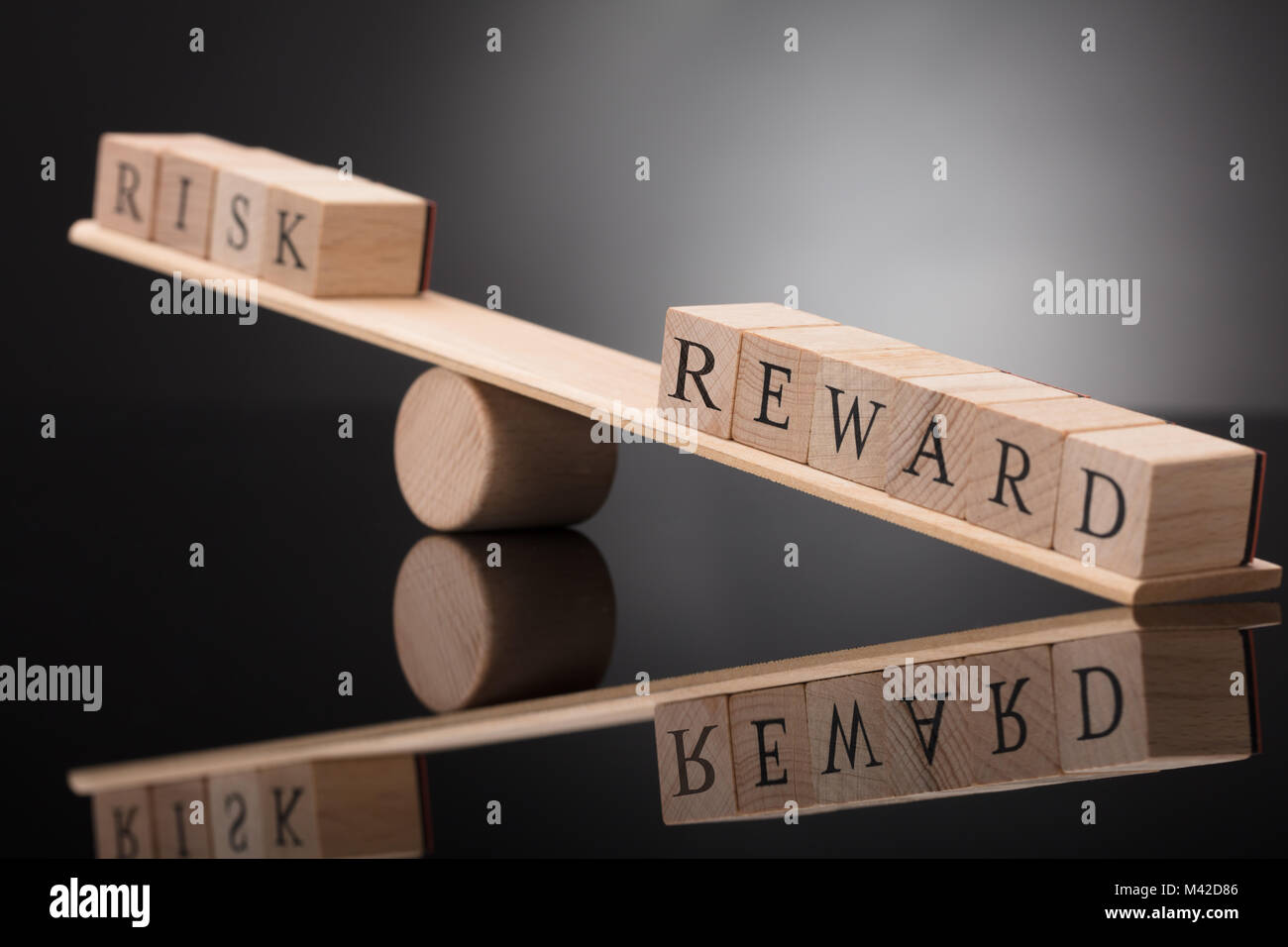 Close-up de un balancín de madera mostrando desequilibrio entre riesgo y recompensa sobre fondo gris Foto de stock