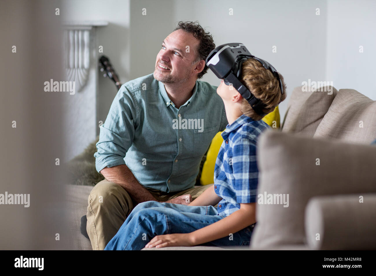 Boy utilizando un auricular VR juego en casa con el Padre Foto de stock