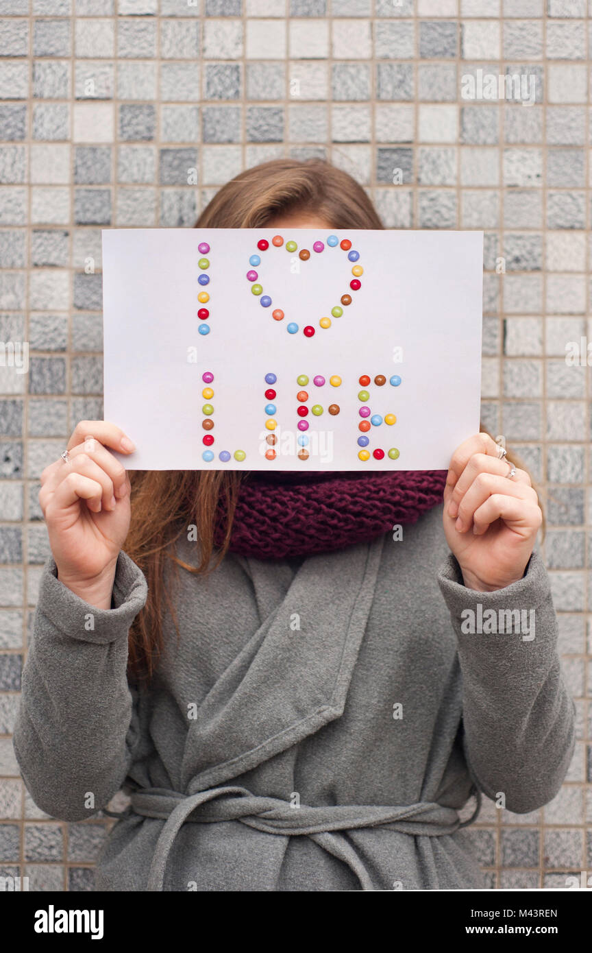 Mujer joven sosteniendo un papel con las palabras "Yo amo la vida" por delante de la cara Foto de stock