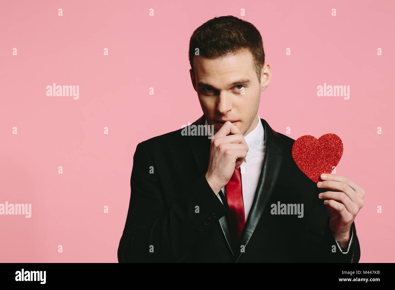 Guapo en un traje negro sosteniendo un corazón rojo para el Día de San Valentín Foto de stock