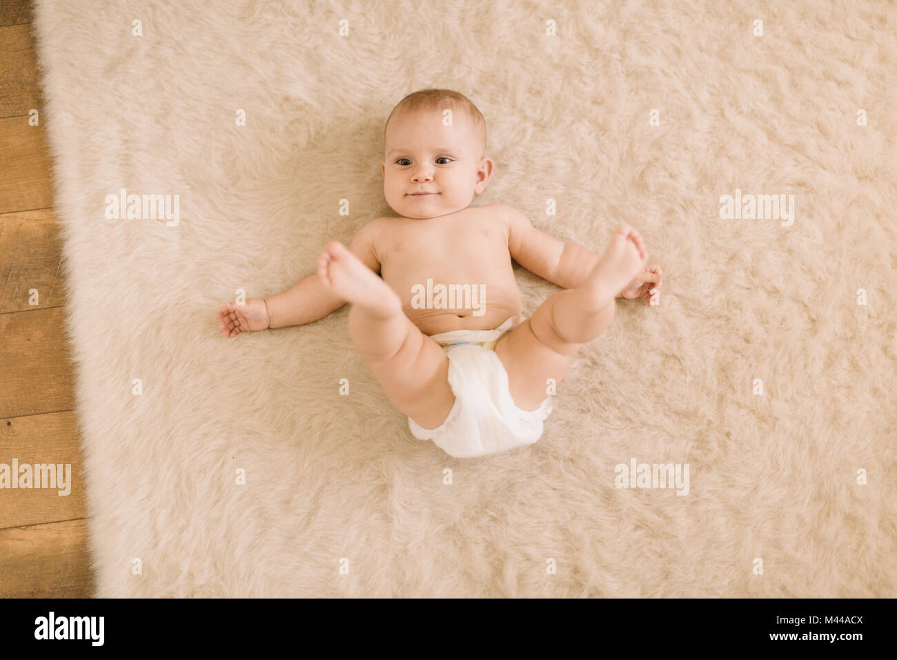Sobrecarga retrato de lindo bebé niña en pañales acostado sobre una alfombra beige Foto de stock
