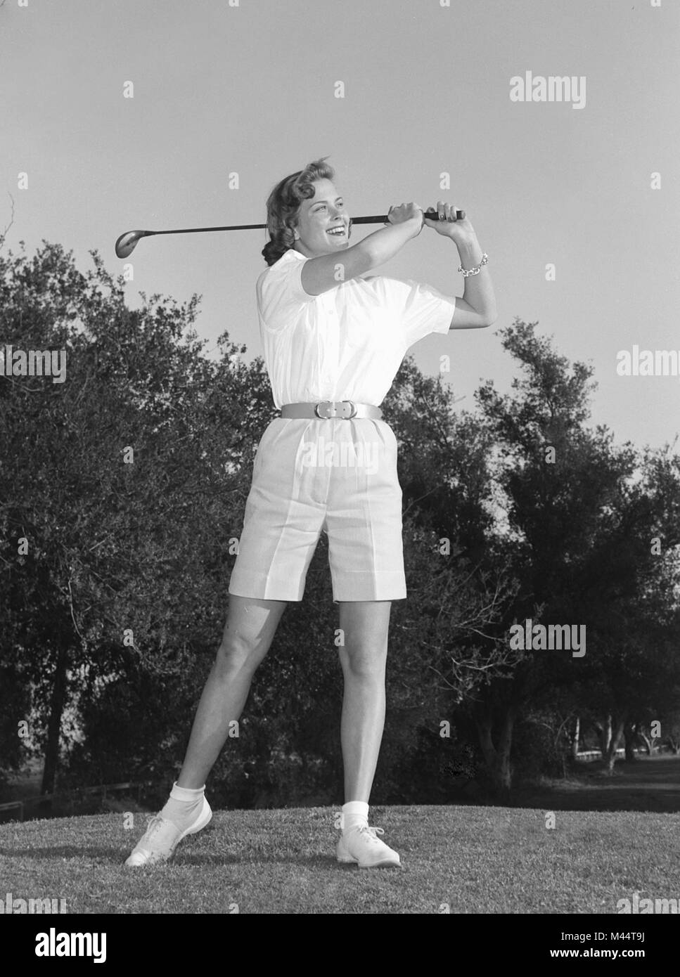 Un golfista femenina impulsa una bola y sonríe al mismo tiempo, ca. 1962. Nombre del archivo: Foto de stock