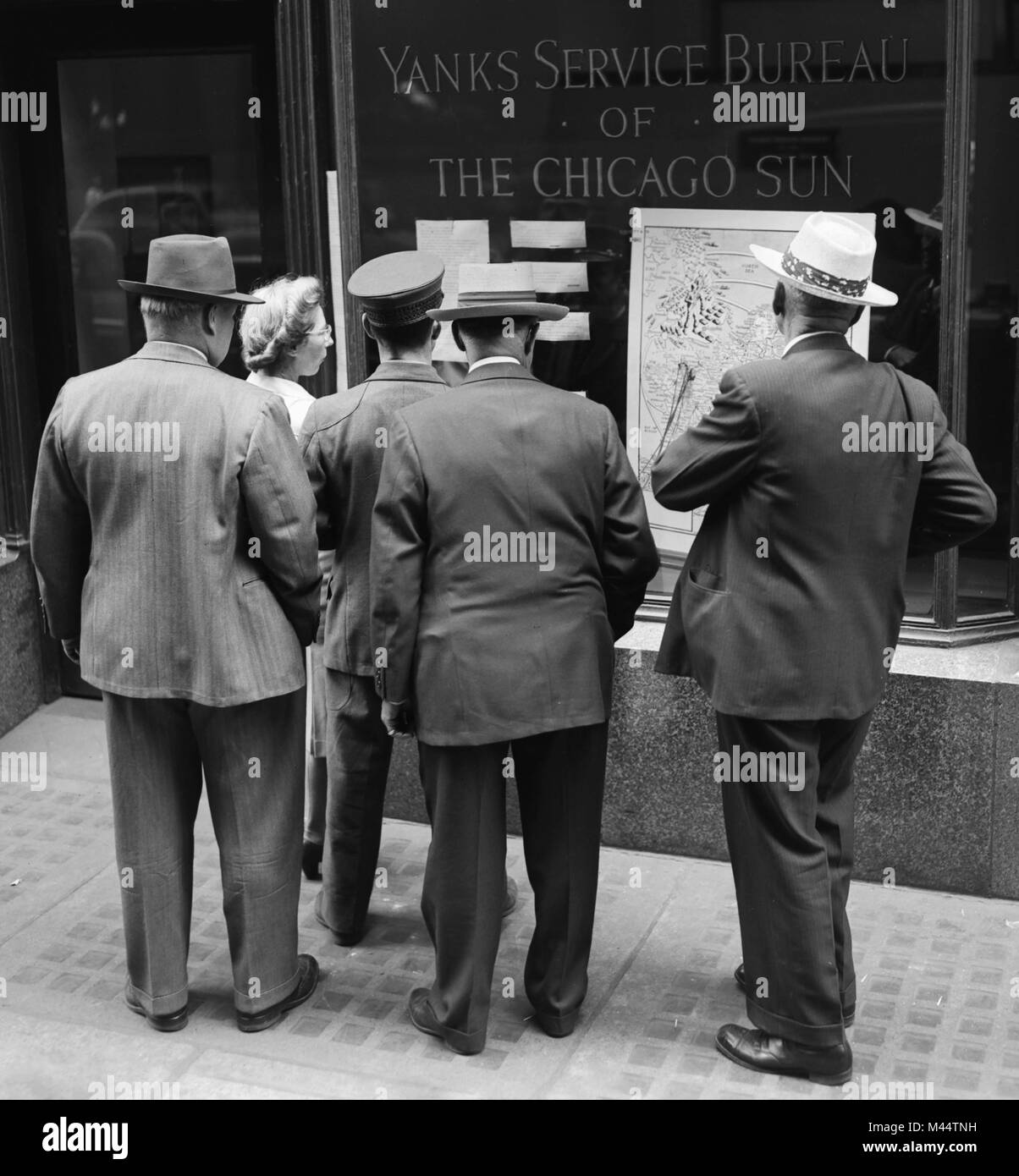 Una multitud se reúne en frente de una actualización de las noticias de la Segunda Guerra Mundial en el Yanks Service Bureau ventana del Chicago Sun, ca. 1944. Foto de stock