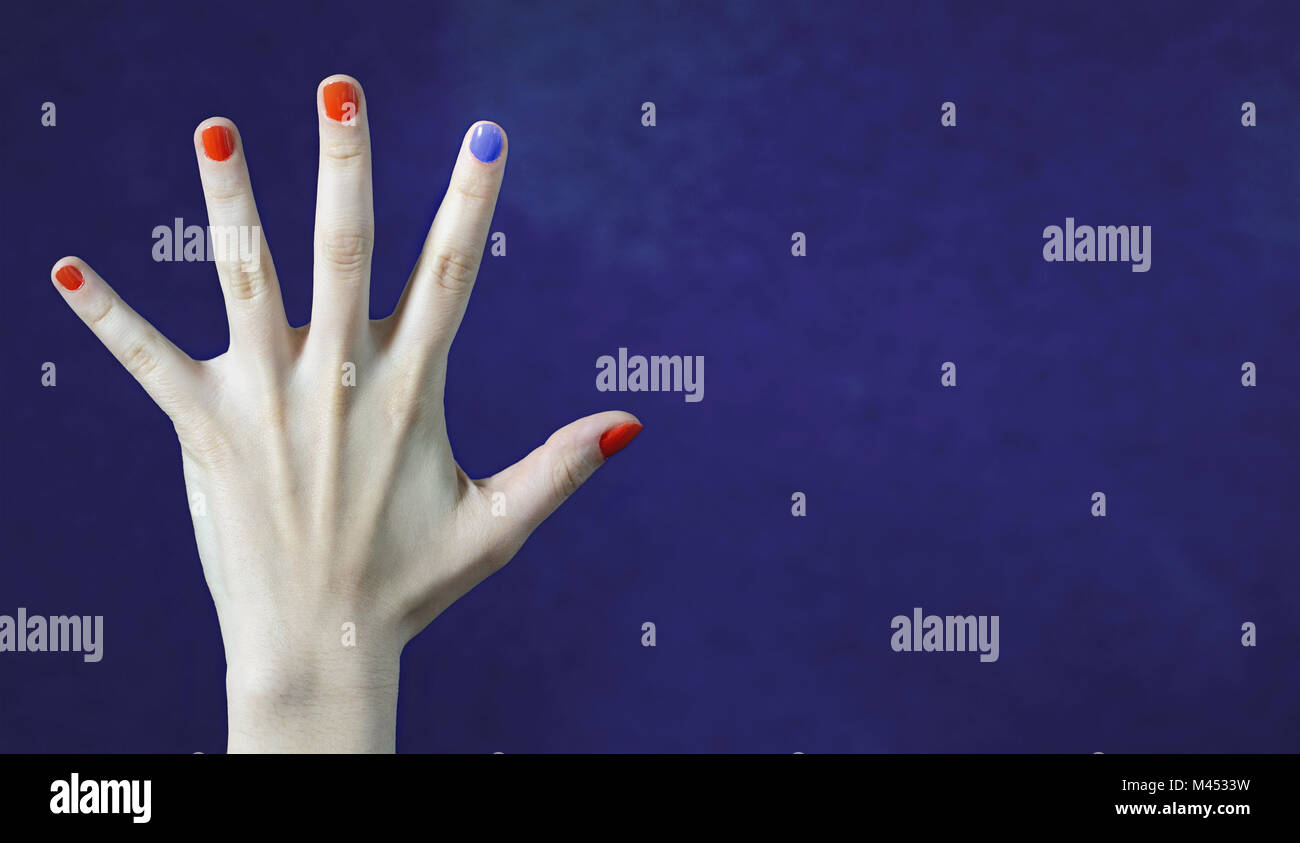 Uno distinto color de uñas en el dedo de la mano del Cáucaso. Las uñas pintadas de rojo y azul. Atrévete a ser diferente, el concepto de originalidad y creatividad. Foto de stock