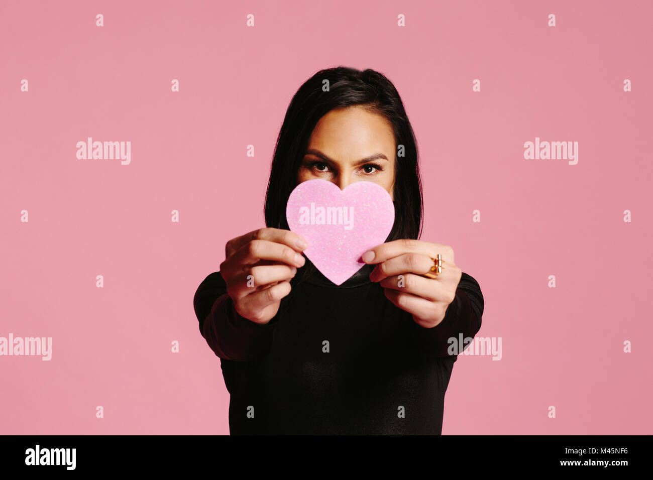 Mujer en negro mostrando pink heart cubriendo la mitad de su cara, mi amor... Foto de stock