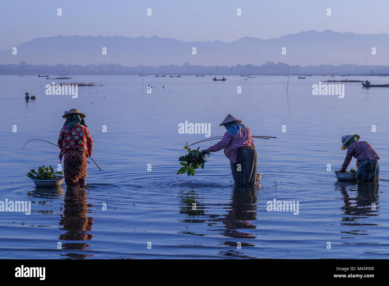 Amanecer sobre el lago con pescadoras pescando en el lago cerca del puente de madera U Bein Puente que cruza el lago Taungthaman cerca de Amarapura en manda Foto de stock