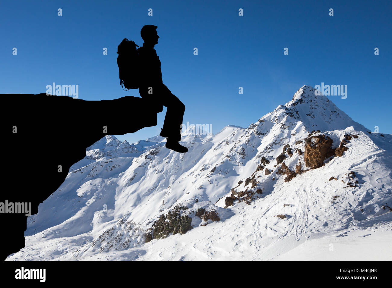 Silueta de un hombre con mochila, sentado en el borde del acantilado explorando ver Foto de stock