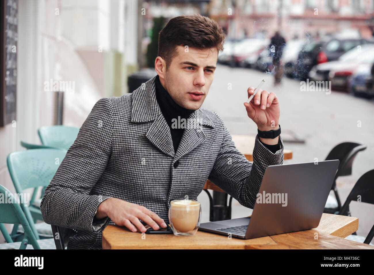 Foto del empresario con elegante aspecto melancólico sentado en el cafe fuera de fumar cigarrillos y beber cappuccino Foto de stock