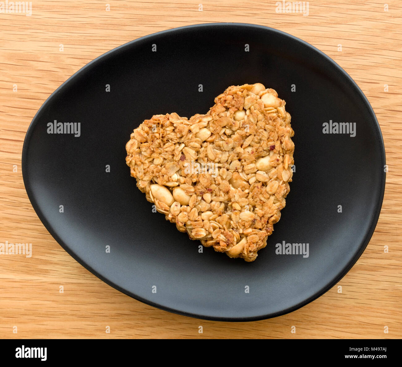 Uno caseras de maní en forma de corazón y avena flapjack galleta fabricada para el día de San Valentín de óvalo placa negra sobre la mesa de madera. Foto de stock