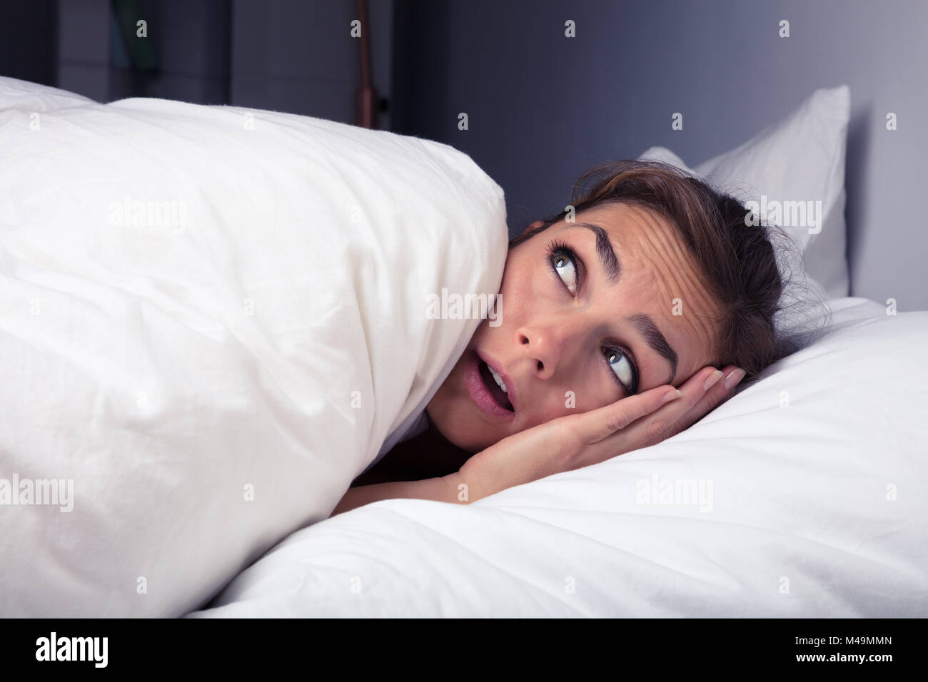 Asustada Mujer tirando de sábana sobre sí mismo en la cama en la noche Foto de stock