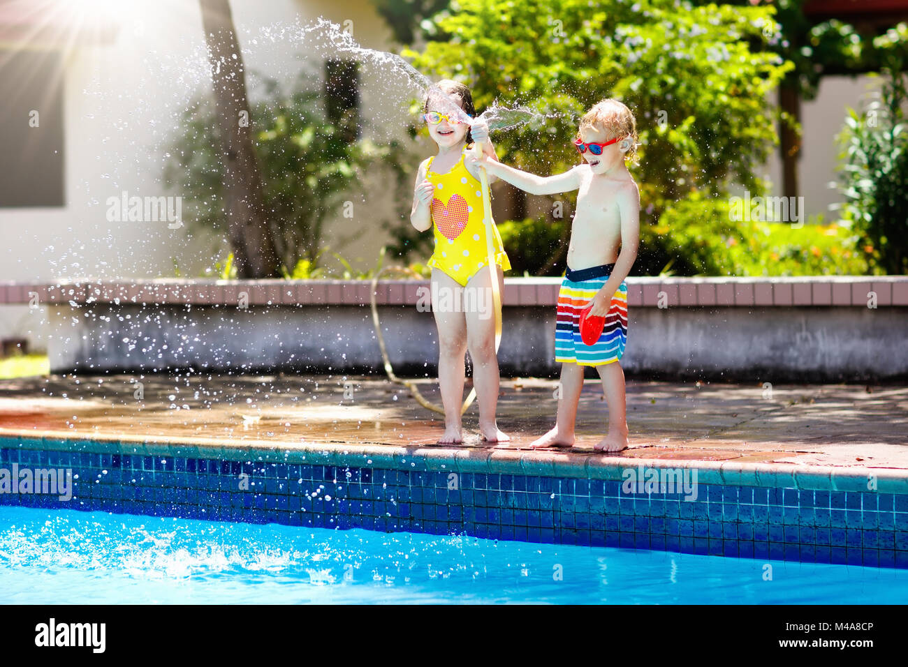 Niños jugando en el patio con una manguera de jardín con una gran piscina  al aire libre. Los niños juegan con agua. Traje de baño y juguetes para  chico y chica. Familia