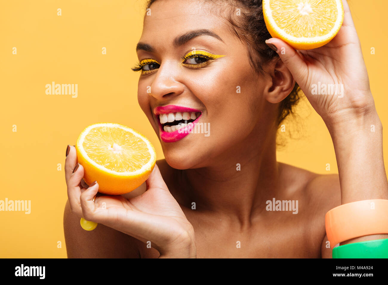 https://c8.alamy.com/compes/m4a924/retrato-de-mujer-mulata-sonriente-con-coloridos-maquillaje-jugoso-sabor-naranja-madura-mantener-partes-en-ambas-manos-cerca-de-la-cara-mas-aislada-pared-amarilla-m4a924.jpg