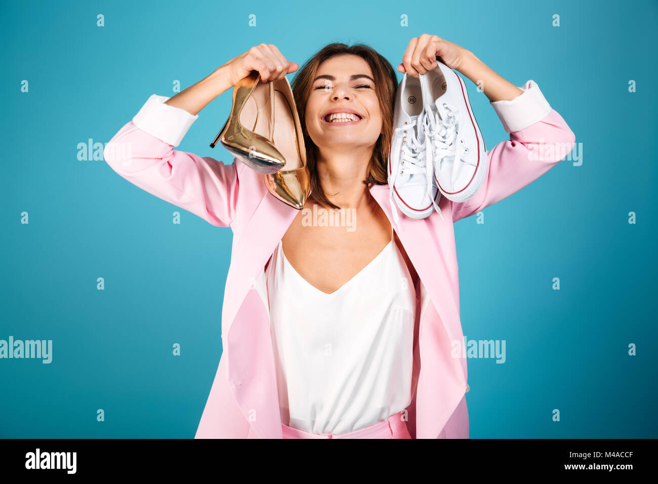Retrato de una mujer vestida encantado en rosa palo sosteniendo par de  zapatos de tacones altos y un par de zapatillas aislado sobre fondo azul  Fotografía de stock - Alamy