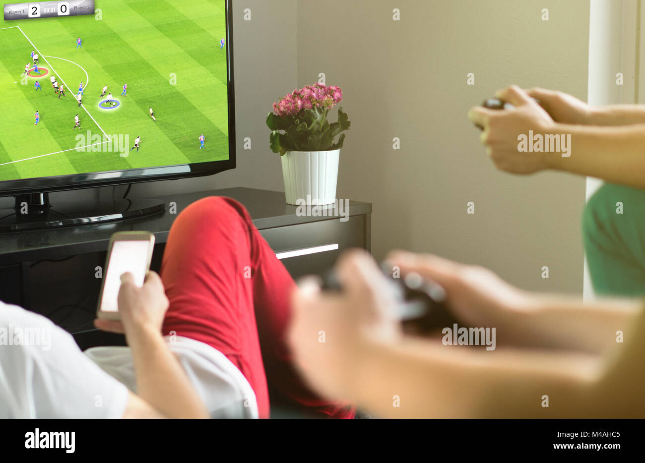 Grupo de sus amigos y jugar fútbol o soccer imaginaria con consola de videojuegos y TV. La noche de los chicos, el partido y el concepto de fin de semana. Foto de stock